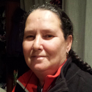 A person with a long braid and a slight smile, wearing a black and red zip-up jacket.