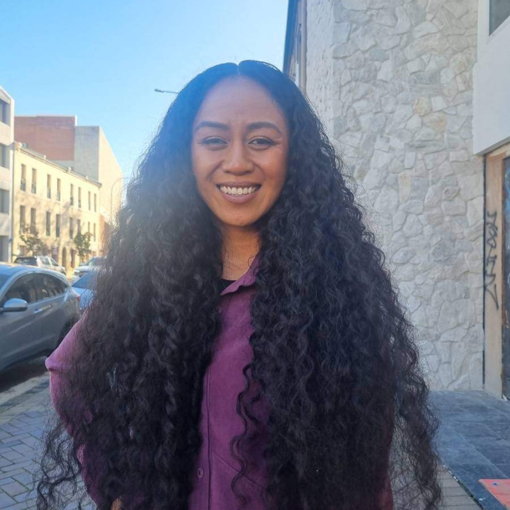 Fran Obicoco smiling in a purple shirt, standing on a city street with long, curly hair