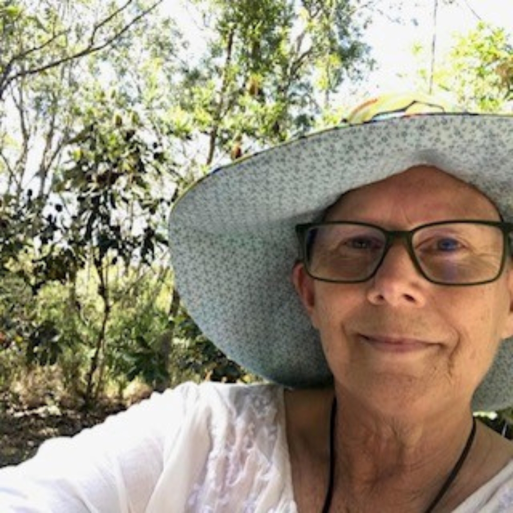 Kerri Shying wearing a light hat and glasses, taking a selfie outdoors among trees.