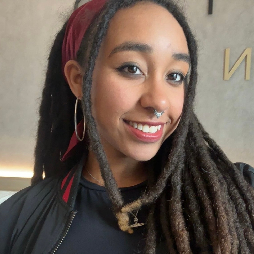 Soul Takawira Joyner smiling, with long locs, a nose ring, and a red head wrap.